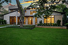 Exterior elevation photo of light gray contemporary home with dark trim, dusk, lights on, green grass and tree in front yard