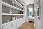 Bathroom with bathtub surrounded by custom backsplash, built-in white dresser, counter with granite countertop and modern fixture