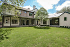 Back of large, modern, two-story, house with green backyard, back porch with pillars, and many windows